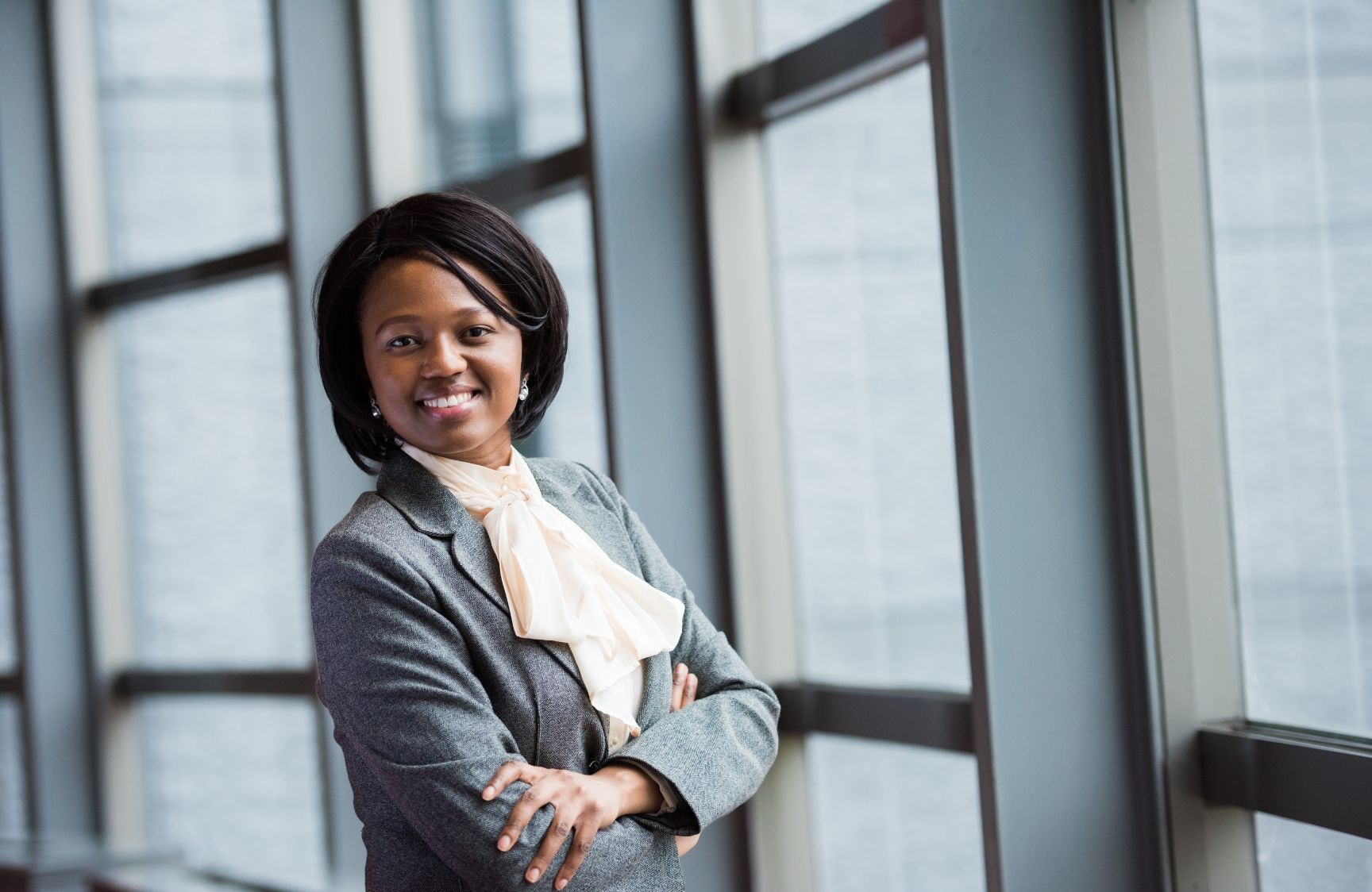 Black business woman smiling and standing with arms crossed in front of large windows