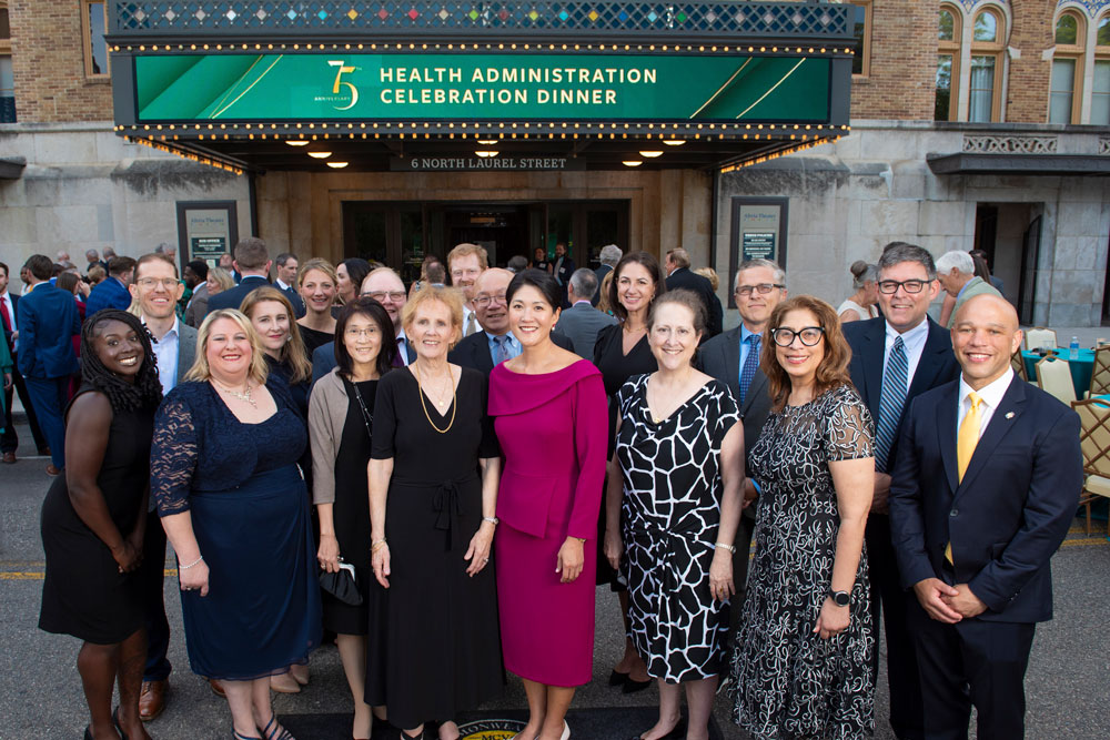 VCU College of Health Professions Health Administration faculty and program leaders pose outside Altria Theater before the program’s celebration dinner, including Beth Williamson Ayers (front row, fourth from left), director of outreach and professional affairs and recipient of the Honorary Alumna Award, and Paula H. Song, Ph.D. (front row, fifth from left), Richard M. Bracken Chair and professor